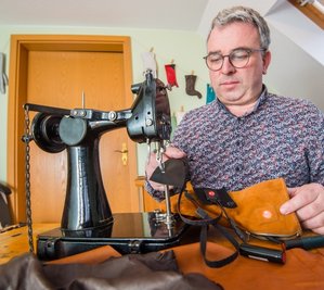 Handschuhmacher Rico Wappler an seiner Nähmaschine. Vor sich hat er einen der Spezialhandschuhe. Der Akku steckt hinter einem Reißverschluss an der Seite, das schwarze Band ist das Heizelement. 