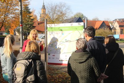 Auf einer Infotafel auf dem Parkplatz am Klein-Erzgebirge in Oederan stehen die Ewilpa-Touren aufgelistet, die Katrin Dechant erklärt.