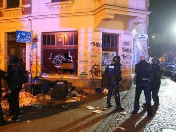 Polizisten vor zerbrochenen Fensterscheiben und verwüsteten Müllcontainern in Leipzig.