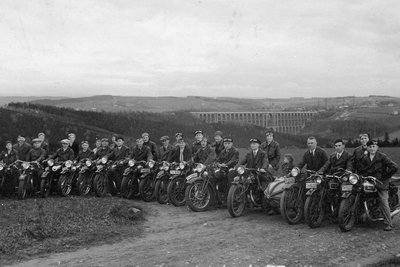 Mitglieder des Motorradklubs Triumph Mylau und Umgebung am 7. Mai 1933 vor einer Ausfahrt ins Waldhotel "Zöbischhaus" in Bad Reiboldsgrün. Die Aufnahme mit Blick auf die Göltzschtalbrücke entstand in Reinsdorf nahe des längst abgerissenen Klublokals "Zur schönen Ausicht". 