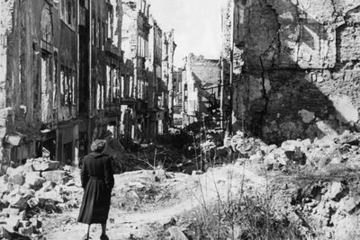 Eine Frau geht in einer Straße in Dresden an Häusern vorbei, von denen nach dem Zweiten Weltkrieg nur noch Ruinen geblieben sind (undatierte historische Aufnahme).