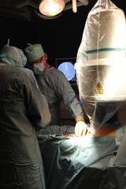 Chefarzt Dr. Wurlitzer (li.) und Oberarzt Dr. Schnee (2.v.li.) während der Gefäßoperation. Rechts ist das Röntgengerät zu sehen, im Hintergrund sieht man auf dem Monitor das Röntgenbild der Gefäße.