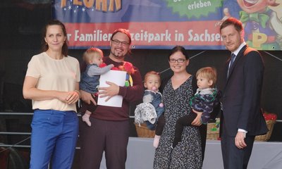 Annett Hofmann (l-r), Ehefrau des sächsischen Ministerpräsidenten Kretschmer, Edgar Kapler, Verena Kapler und ihre Drillinge aus Leipzig, sowie Michael Kretschmer, Ministerpräsident des Landes Sachsen, stehen im Freizeitpark Plohn im Vogtland auf einer Bühne. Dort wurden Patenschaften des Ministepräsidenten für neu hinzugekommene Drillinge übergeben.