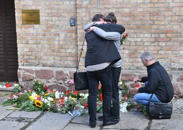 Menschen trauern vor Kerzen und Blumen an der Synagoge. 
