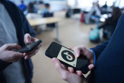 Schüler stehen in einem Klassenraum und schauen auf ihre Smartphones.