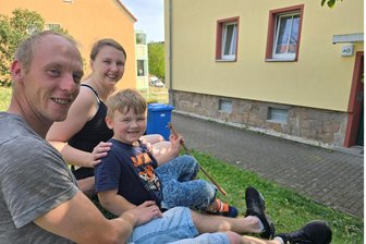 70 Jahre Wohnungsgenossenschaft Crimmitschau: Warum eine junge Familie nicht ans Wegziehen denkt - Haben auf dem Rasen vor dem Wohnhaus ein kühles Plätzchen gefunden: Sarah Klitzsch und Sven Stößel mit Sohn Elias. Die junge Familie liebt die Ruhe und die modern sanierte Wohnung. Sie sind zufrieden: Die Hausmeister der Wohnungsgenossenschaft bringen sogar die Mülltonnen an die Straße.