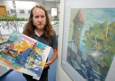 Mario Schmidt mit dem Bild "Im wunderlich wilden Wandel der Zeit" in der Hand. Das rechte Bild heiß "Das altbekannte Spiel". 