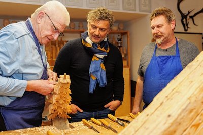 Jonas Kaufmann (M.) schaute bei den Dreharbeiten in der Schnitzschule mit Leiter Volker Krämer (r.) Gunter Dziubale zu. 