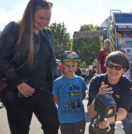 Jessica Eltner informiert sich mit dem noch etwas skeptisch dreinschauenden Junior Levi, der mit dem Gedanken spielt, in die Kinderfeuerwehr einzutreten, bei Markus Heiduk vom THW über die Wärmebildkamera. 