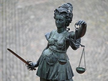            Die Statue der Justitia steht mit einer Waage und einem Schwert in der Hand.