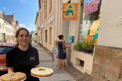 Celine Zenner auf dem Weg von der „Heldenstube“ zum Café Mehrwert um die Ecke. Hinter Heldenstube und Café liegt der neue Mitmachgarten - leicht erreichbar über den Tischendorfplatz. In der „Heldenstube“ ist nicht nur Platz für Kuchenproduktion und Workshops - davor hängt ein Briefkasten, in dem stets Post mit neuen Ideen willkommen ist.