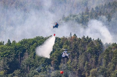Hubschrauber der Bundespolizei fliegen mit einem Löschwasser-Außenlastbehälter über den Nationalpark.