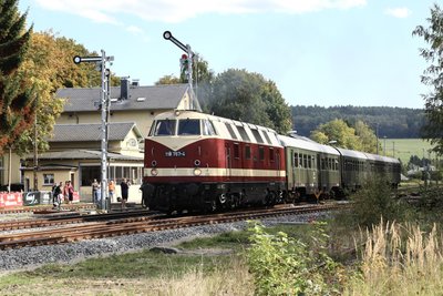 Eine Diesellok der Baureihe 118 der Reichsbahn, die heute bei der Preßnitztalbahn im Einsatz ist, fährt mit einem Personenzug nach Schwarzenberg aus dem Bahnhof Schlettau aus.