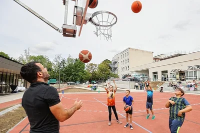 Sportlehrer Paul Ogorsolka testet mit den Schülern Pia, Tom, Toni und Phil (von links, alle Kinder sind acht Jahre) schon einmal das neue multifunktionale Spielfeld der DPFA-Regenbogenschule mit einer Runde Basketball. 