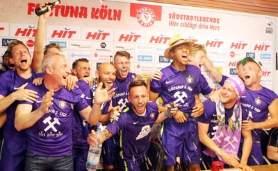 Mit Gebrüll, Getränken, Aufstiegs-T-Shirts und lauter Musik stürmt die Mannschaft die obligatorische Pressekonferenz nach dem Spiel.