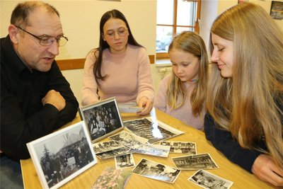 Schalmeienchef Uwe Schamberg zeigt Lena Westermann, Mia-Katrin Kiesow und Jenny Hardwich schwarz-weiß Fotos aus früherer Zeit.