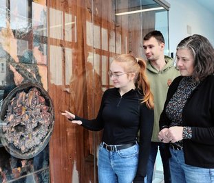 BSZ-Schulleiterin Caterina Martin (r.) sieht sich mit der Dorfchemnitzerin Lorena Weidlich (20), die im 3. Ausbildungsjahr zur Kauffrau für Büromanagement ist, und dem Crandorfer Max Gräßler (17) aus der Klasse 12 der Fachoberschule die wieder aufgebaute "Brockhage-Wand" an. 