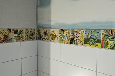 Blick in einen Sanitärraum im Werkstatt-Neubau - mit den Fliesen-Bordüren aus der Druck- und Kreativ-Werkstatt der Lebenshilfe.