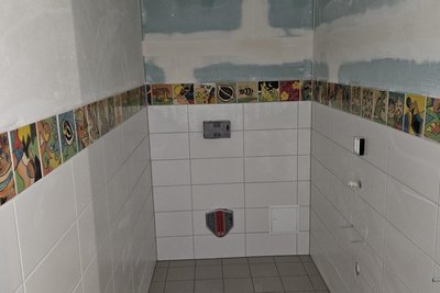 Blick in einen Sanitärraum im Werkstatt-Neubau - mit den Fliesen-Bordüren aus der Druck- und Kreativ-Werkstatt der Lebenshilfe.