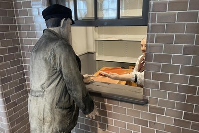 In einer nachgebauten Lohnschalterhalle „sprechen“ die vor dem Schalter stehenden Figuren „miteinander“.