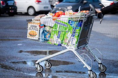 Ein Kunde schiebt einen bis zum Rand gefüllten Einkaufswagen über den Parkplatz eines Supermarktes.