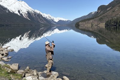 Beim Angeln spiegeln sich die Berge im klaren Wasser.