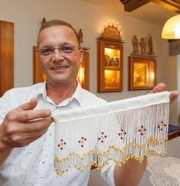 Was einst in vielen Stuben in Heimarbeit gefertigt worden ist, ziert nun auch Fenster im Turmmuseum Geyer. Leiter Lutz Röckert hat Perlfransengardinen bei Vorführungen angefertigt, passend zum Jubiläum. Foto: Ronny Küttner