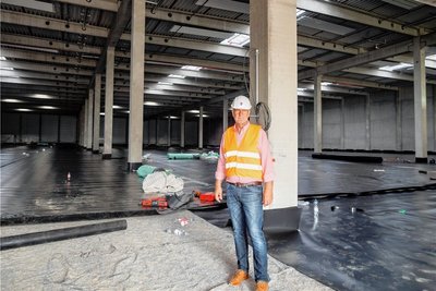 Christian Halpick in einer noch nicht fertigen Halle, deren Boden mit Folie versiegelt wird. 