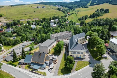 Der Komplex aus denkmalgeschützter Mittelschule (rechts) sowie der erst deutlich später errichteten Turnhalle und der Grundschule aus der Luft. Links ist zudem der Garagen- und Containerstandort zu sehen, den die Stadt nun auch an den Investor verkauft.