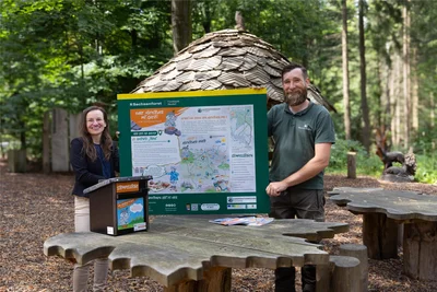 An 13 Ausflugszielen in der Greifensteinregion können Kinder neuerdings mit Greifis Abenteuerpass Stempel sammeln. Eine Stempelstelle ist im Abtwald zu finden. Hier zeigen Tourismuskoordinatorin Corinna Bergelt und Revierförster Tobias Hamm am beliebten Rastplatz „Tisch´l“ die Infotafel und die Stempelstelle.