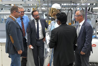 Wissenschaftsminister Sebastian Gemkow (M.) lässt sich im Helmholtz Institut Freiberg die Schutzbekleidung erklären.