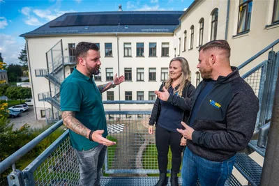 Steve Beyer (l.) ist Energiemanager der Stadt Eibenstock. Er schaut sich gemeinsam mit Nadja Kaulfuß und Tobias Mann von der Firma Clen Solar die PV-Anlage an, die auf dem Dach der Oberschule installiert wurde.