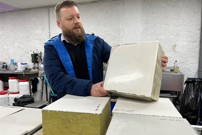 Benjamin Hiller betrachtet einen Mineralfaserblock mit der zementbasierten Beschichtung.