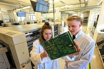 Mitarbeiterin Saskia Pfeil und Azubi Vincent Pehns kontrollieren eine Leiterplatte für Telekommunikationsgeräte, die in Hartmannsdorf bestückt wird.