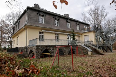 An Details wie Natursteinsockel, Freitreppe und Terrasse ist zu erkennen, dass es sich bei dem Gebäude um eine einstige Fabrikantenvilla handelt.