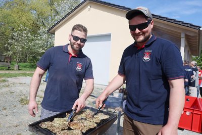 Philip Wunder (l.) und Christopher Pomper von der Ortswehr waren zur Einweihung der Vereinsremise (hinten) als Grillmeister im Einsatz.