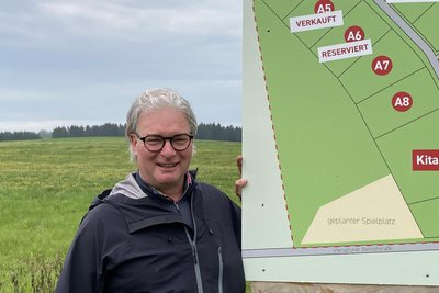 Noch ist überall grüne Wiese, doch schon bald rollt schweres Baugerät an. Investor Markus Lux an der Schautafel zum Baugebiet „Hauptmannsgrüner Straße“ in Irfersgrün.