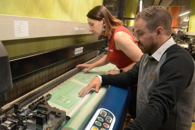 Produktionsleiter Thomas Baumann und Weberin Monika Czerkieska kontrollieren die Ware auf Fehler. Hier wurde es probehalber mit grünem Garn gewebt. Original gibt es das Tuch in Rot.