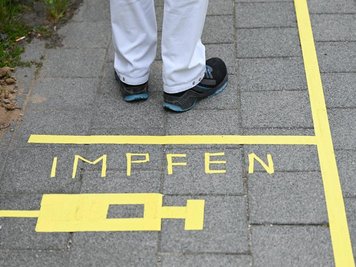            Ein Mann steht am Covid-19 Impfcenter hinter einer Bodenmarkierung mit der Aufschrift "Impfen" und einer Spritze.