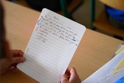 Ein Symbolbild: Ein Grundschüler aus der Ukraine hält im Deutschunterricht einen Zettel mit Schreibübungen in der Hand.