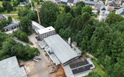 Das Eisenwerk Elterlein aus der Vogelperspektive. Das Hallendach in der Mitte ist für die Aufnahme der Solarmodule vorbereitet, zu erkennen an den silbrig schimmernden Montageschienen. 