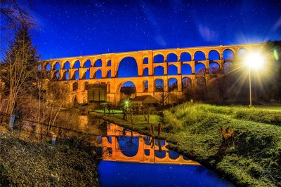 Langzeitbelichtung: Die nachts angestrahlte Brücke spiegelt sich im Wasser des Mühlgrabens.