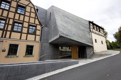 Gekrümmt, vom Wasser umspielt und einer rauen Muschelschale nachgebildet: Der viel diskutierte Zwischenbau aus wuchtigem Sichtbeton zwischen Fachwerk prägt die Ansicht des Erlebnismuseums Perlmutter.