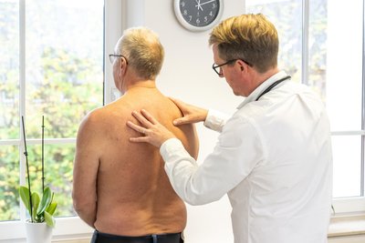 Ein Arzt tastet den Rücken eines Patienten ab.