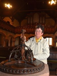 Evelyn Ziegelt, kirchliche Mitarbeiterin, am Taufstein in der Schwarzbacher Kirche. Orgel und Glockengeläut sollen überholt werden.