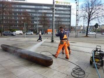 Die Holzbänke vorm Archäologiemuseum werden mit einem Hochdruckreiniger gesäubert.