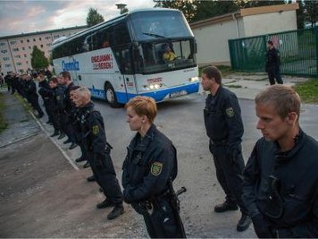 Polizisten stehen vor einem Bus, der Flüchtlinge in eine Notunterkunft bringt.