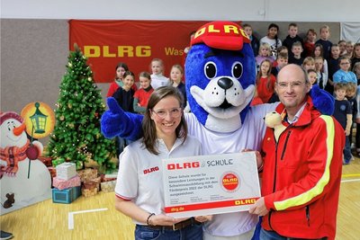 Lehrerin Anja Haberkorn und DLRG-Landespräsident Andreas Lorenczat freuen sich mit Maskottchen Nobbi über den Förderpreis.