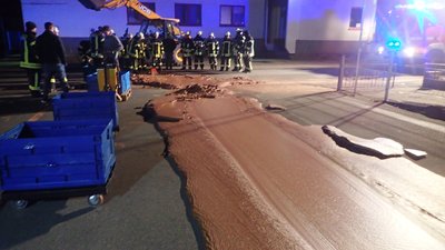 Einsatzkräfte der Feuerwehr stehen neben auf der Strasse ausgelaufener Schokolade. Ein Schokoladentank war bei einer Firma übergelaufen. Die Strasse wurde gesperrt, eine Tonne Schokolade musste von einer Fachfirma beseitigt werden.