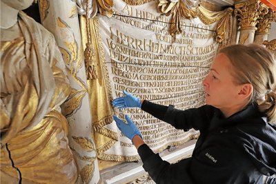 Diplom-Restauratorin Silvia Oertel an dem stark beschädigten Holzeptiaph für Heinrich Schmidt. Einst aus einzelnen Bretter zusammengesetzt, klaffen diese jetzt teils weit auseinander. 